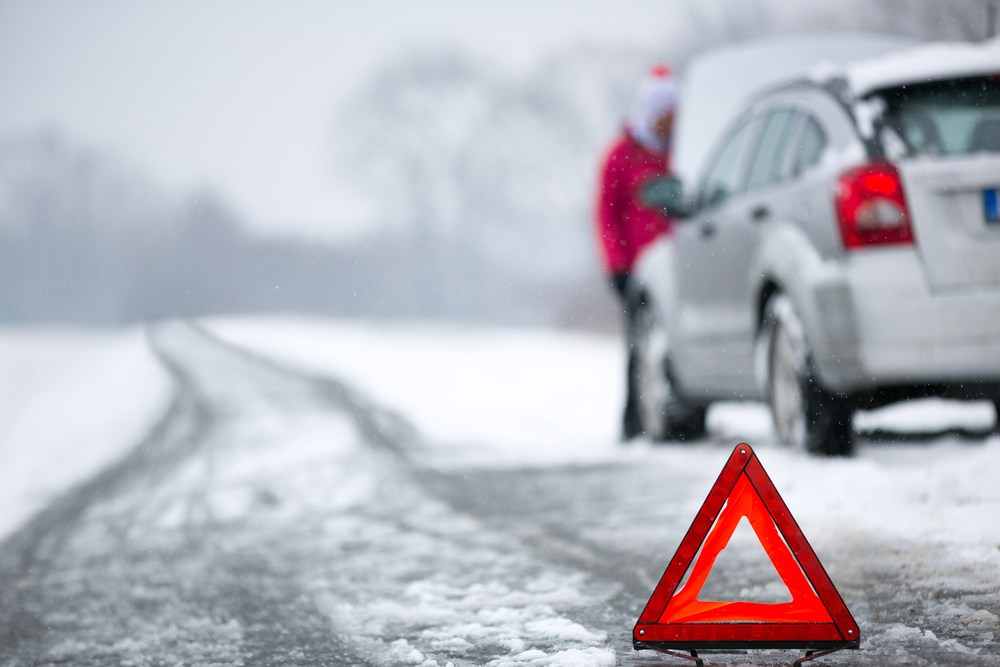 Woman standing next to stalled car in winter in ontario