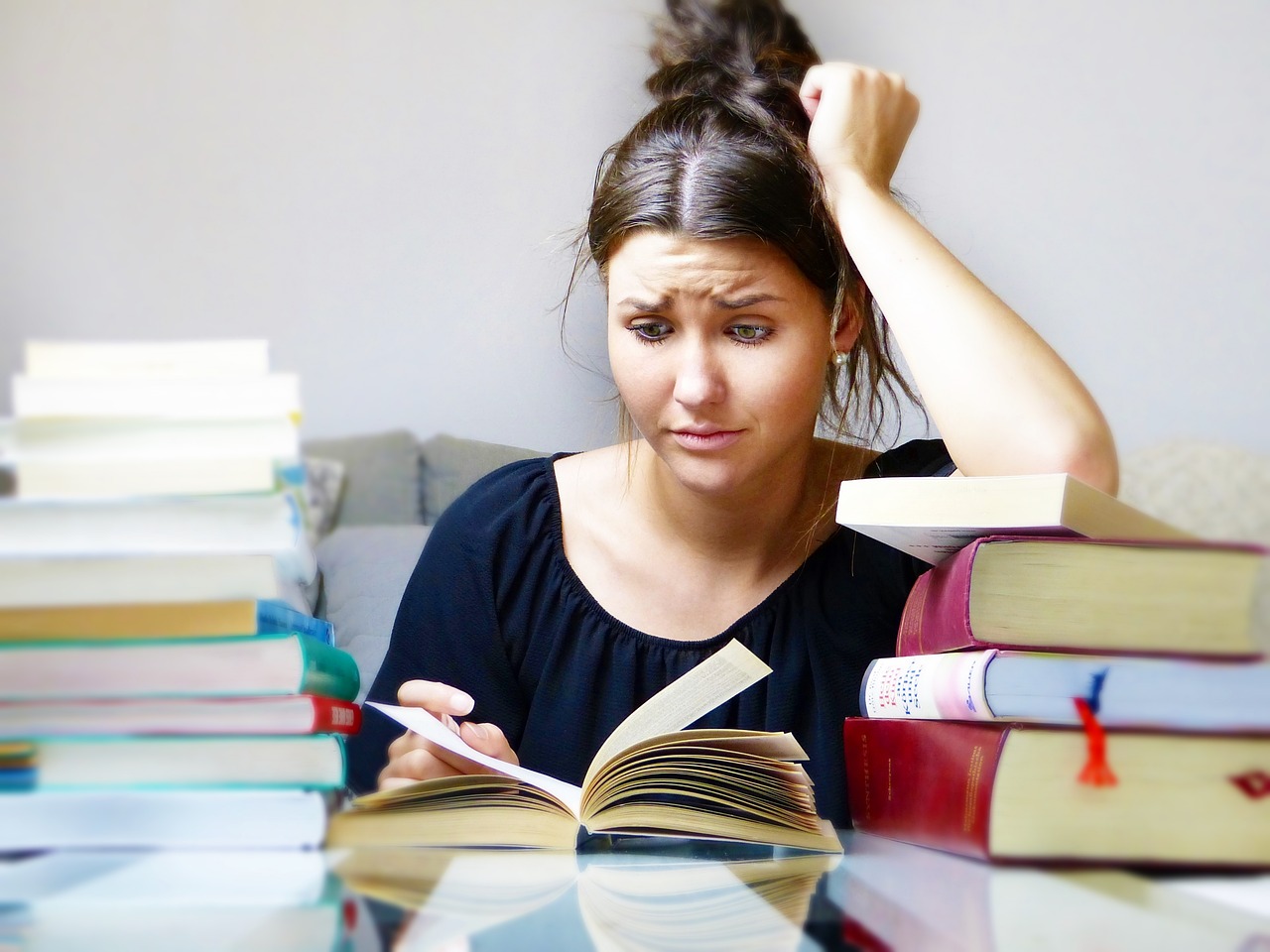 A girl reading a lot of books, looking stressed.